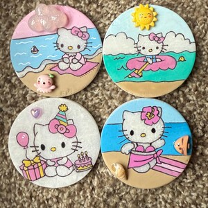 Op de afbeelding: Vier ronde keramische onderzetters met Hello Kitty in verschillende zomerse sc&egrave;nes. De onderzetters zijn geschilderd met Hello Kitty in een badpak, een zwemband, een verjaardagshoed en een wolk. Elke onderzetter heeft een andere achtergrondkleur en bevat andere zomerse details.