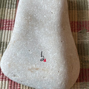 Puede incluir: Una piedra gris con una nota musical negra y un coraz&oacute;n rojo pintado en ella.