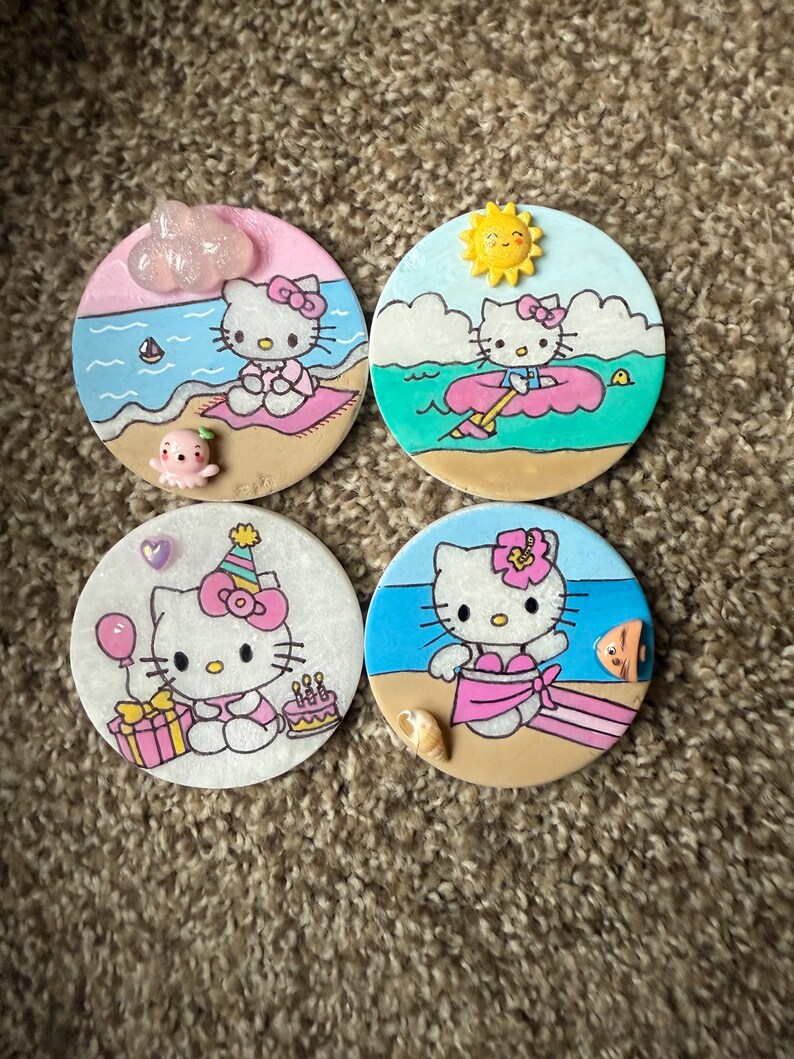 Op de afbeelding: Vier ronde keramische onderzetters met Hello Kitty in verschillende zomerse sc&egrave;nes. De onderzetters zijn geschilderd met Hello Kitty in een roze badpak, een roze zwemband, een verjaardagshoed en een roze bikini. Elke onderzetter heeft een andere achtergrondsc&egrave;ne.