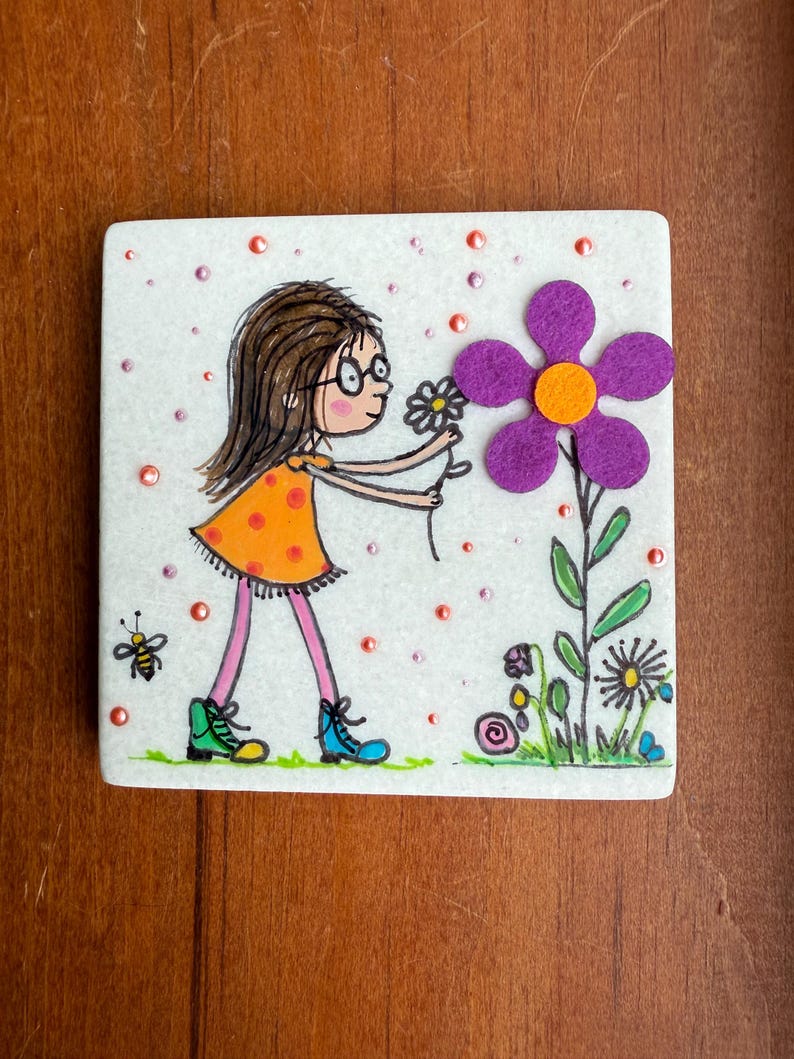Puede incluir: Azulejo de cer&aacute;mica cuadrado con una ilustraci&oacute;n de dibujos animados de una ni&ntilde;a con un vestido naranja recogiendo una flor. A la derecha hay una gran flor morada con un centro naranja. Tambi&eacute;n se representa una abeja y otras flores.