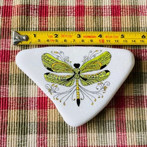 K&ouml;nnte beinhalten: Ein wei&szlig;er dreieckiger Stein, der mit einer gr&uuml;nen und gelben Libelle mit schwarzen Umrissen bemalt ist. Die Libelle hat komplizierte Details und ein schwarzes Herz in der Mitte ihres K&ouml;rpers.