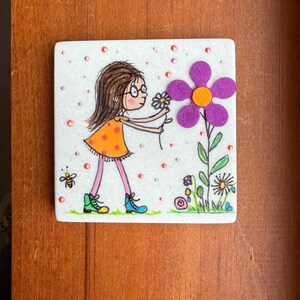 Puede incluir: Ilustraci&oacute;n cuadrada dibujada a mano de una ni&ntilde;a con gafas con un vestido naranja, sosteniendo una peque&ntilde;a flor. A la derecha hay una gran flor morada con un centro naranja. Tambi&eacute;n se representan una abeja y otras flores.