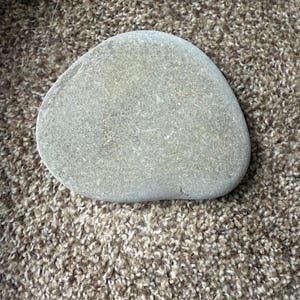 Puede incluir: Una piedra de r&iacute;o lisa y gris con forma redondeada. La piedra tiene una superficie ligeramente texturizada y diferentes tonos de gris. La piedra es un elemento natural.