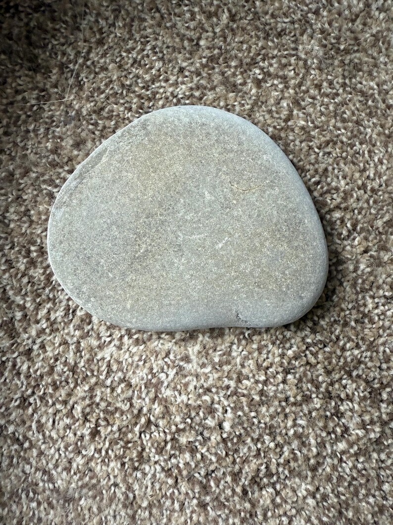 Puede incluir: Una piedra de r&iacute;o lisa y gris con forma redondeada. La piedra tiene una superficie ligeramente texturizada y diferentes tonos de gris. La piedra es un elemento natural.