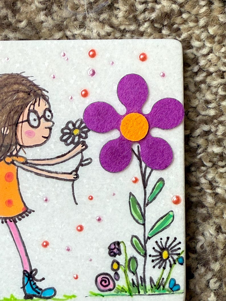 Puede incluir: Una ilustraci&oacute;n caprichosa presenta a una ni&ntilde;a con un vestido naranja y zapatos azules ofreciendo una flor a una gran flor de fieltro morado con un centro naranja. El fondo es blanco con peque&ntilde;os puntos rosas y naranjas y otras flores dibujadas.