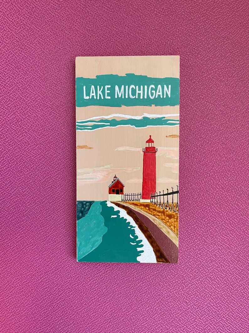 K&ouml;nnte beinhalten: Ein Holzschild mit einem gemalten Bild eines roten Leuchtturms auf einem See mit dem Text "LAKE MICHIGAN" oben.