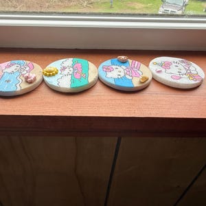 Op de afbeelding: Vier ronde onderzetters met een witte achtergrond en kleurrijke afbeeldingen van Hello Kitty op een strandthema. De onderzetters zijn versierd met kleine, kleurrijke versieringen.