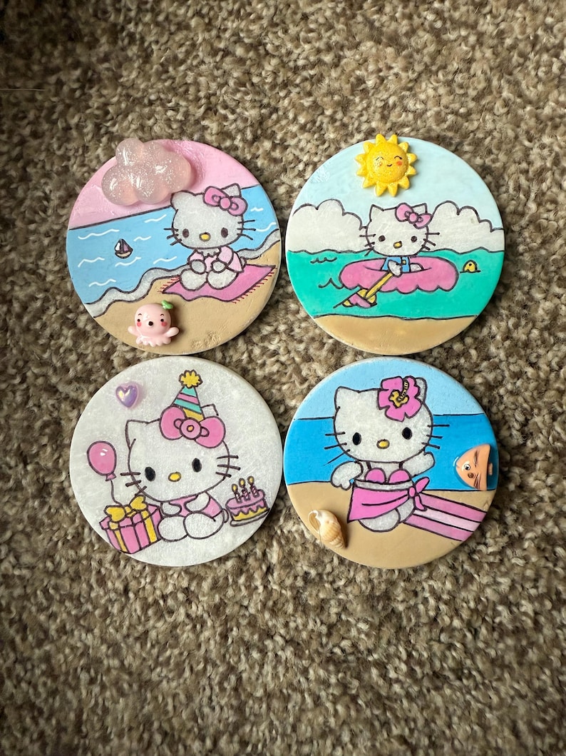 Op de afbeelding: Vier ronde onderzetters met Hello Kitty in verschillende zomerse taferelen. De onderzetters zijn wit met een lichtroze, blauwe of gele achtergrond. Hello Kitty draagt een badpak, een zwemvest, een verjaardagshoed en een roze jurk. De onderzetters zijn versierd met schelpen, een zeilboot, een zon en een verjaardagstaart.
