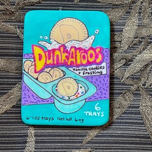 May include: A teal blue box with a white and yellow logo that says "Dunkaroos" and a picture of vanilla cookies and frosting. The box says "6-1oz trays Net Wt. 603 6 TRAYS".