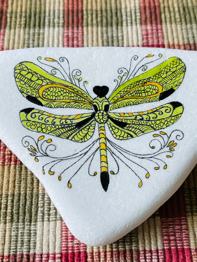 K&ouml;nnte beinhalten: Ein handbemalter Stein mit einem detaillierten gr&uuml;nen und gelben Libellen-Design. Die Libelle hat schwarze Akzente und komplizierte Muster auf ihren Fl&uuml;geln.