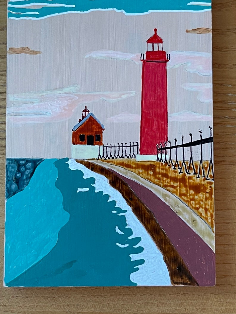 K&ouml;nnte beinhalten: Ein Gem&auml;lde, das einen roten Leuchtturm mit einem kleineren braunen Geb&auml;ude daneben zeigt. Der Leuchtturm steht auf einem Pier mit einem Holzzaun. Das Wasser ist blau und es gibt wei&szlig;e Wellen. Der Himmel ist rosa und wei&szlig;.