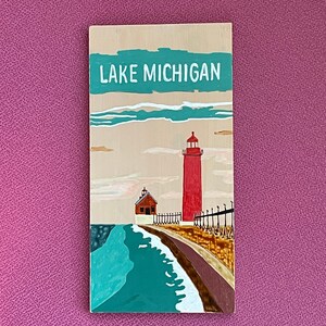 K&ouml;nnte beinhalten: Ein Holzschild mit dem Text "LAKE MICHIGAN" in wei&szlig; auf einem t&uuml;rkisfarbenen Hintergrund. Das Schild zeigt einen roten Leuchtturm mit einem wei&szlig;en Dach und ein kleineres wei&szlig;es Geb&auml;ude mit einem roten Dach. Der Leuchtturm steht auf einem Steg mit einem braunen Holzgel&auml;nder. Das Wasser ist t&uuml;rkisfarben mit wei&szlig;en Wellen.