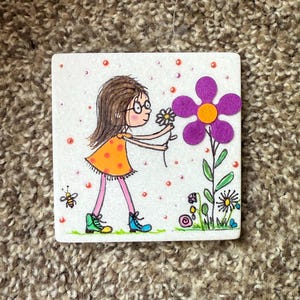 Puede incluir: Azulejo de cer&aacute;mica cuadrado con una ilustraci&oacute;n de dibujos animados de una ni&ntilde;a con un vestido naranja y botas azules recogiendo una flor. Tambi&eacute;n se representa una abeja y otras flores.
