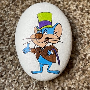 Puede incluir: Piedra pintada a mano con un rat&oacute;n de dibujos animados que lleva un sombrero de copa morado y verde, una chaqueta marr&oacute;n y pantalones azules. El rat&oacute;n sostiene un bast&oacute;n en su mano derecha y tiene una expresi&oacute;n de sorpresa en su rostro.
