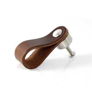 May include: A brown leather cabinet pull with a silver metal base and screw. The leather is folded over to create a loop for pulling.
