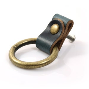 May include: A teal leather drawer pull with a brass ring and a brass screw. The leather is folded over to create a loop.