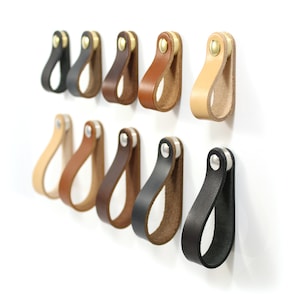 May include: Assortment of leather drawer pulls in various colors, including brown, black, tan, and natural. Each pull has a single metal screw for mounting.
