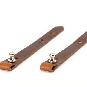May include: Two brown leather straps with metal snaps. Each strap has four holes.