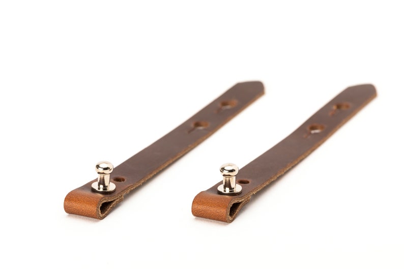 May include: Two brown leather straps with metal snaps. Each strap has four holes.