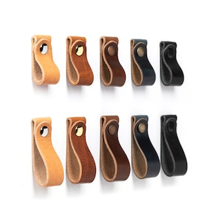 May include: Ten leather cabinet pulls in various colors, including brown, tan, black, and blue. Each pull has a simple, curved design and a brass accent.