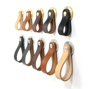 May include: Assortment of leather cabinet pulls in various colors, including black, brown, tan, and cream. The pulls are attached to a metal base with a screw.