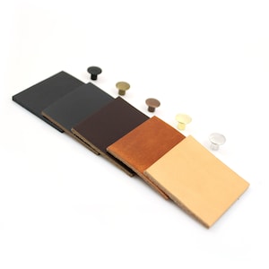 May include: Five leather swatches in different colors: black, brown, orange, beige, and white. Each swatch is accompanied by a small metal rivet in a matching color.