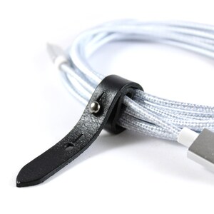 May include: A close-up of a black leather cable organizer with a silver button. The organizer is wrapped around a silver and white braided cable.