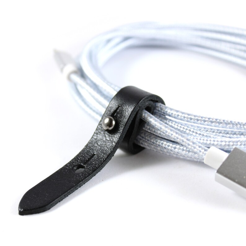 May include: A close-up of a black leather cable organizer with a silver button. The organizer is wrapped around a silver and white braided cable.