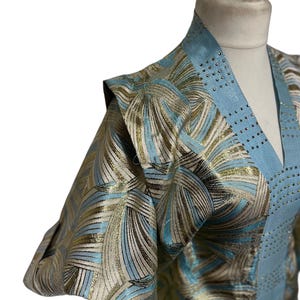 Pode incluir: Uma túnica azul claro e dourada com padrão, decote em V e mangas compridas. A túnica tem uma guarnição decorativa de strass.