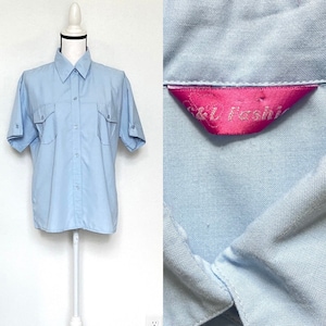 Puede incluir: Camisa azul claro de manga corta con dos bolsillos en el pecho y cuello. La camisa se muestra en un maniquí blanco. La etiqueta dentro de la camisa dice "S & L Fashion".