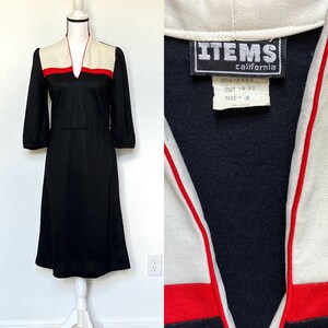 May include: A black dress with white and red trim. The dress has a V-neck and long sleeves. The label on the dress reads "ITEMS California, Style 3-480, Cut 8-32, Size 8."