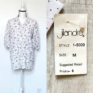 May include: White shirt with a pattern of red and blue floral designs. The shirt is size M and has short sleeves. A tag reads "jilandré" and "STYLE: 1-5000".