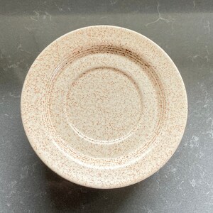 May include: A beige saucer with a speckled pattern and a raised center.