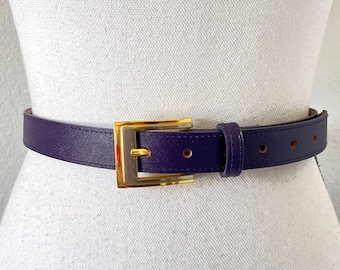 May include: A purple leather belt with a gold buckle. The belt is on a white mannequin.