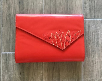 Könnte beinhalten: Eine leuchtend rote Clutch mit einem dekorativen Design aus goldenen und roten Pailletten.