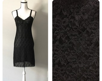 Puede incluir: Un vestido de encaje negro con un dobladillo festoneado. El vestido está en un maniquí blanco y tiene un diseño simple y elegante.