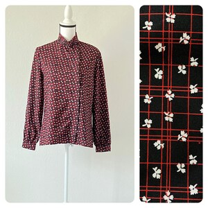 May include: A red and white patterned blouse with a high collar and long sleeves. The pattern features small white dots on a red background with a subtle plaid design.