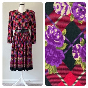 Puede incluir: Un vestido de manga larga con estampado floral negro, rojo y morado. El vestido tiene un corpiño ajustado y una falda completa. La tela es un tejido suave y elástico.