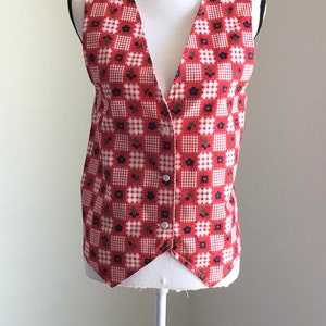 May include: A red and white gingham vest with a floral pattern and a button closure. The vest is sleeveless and has a V-neck.