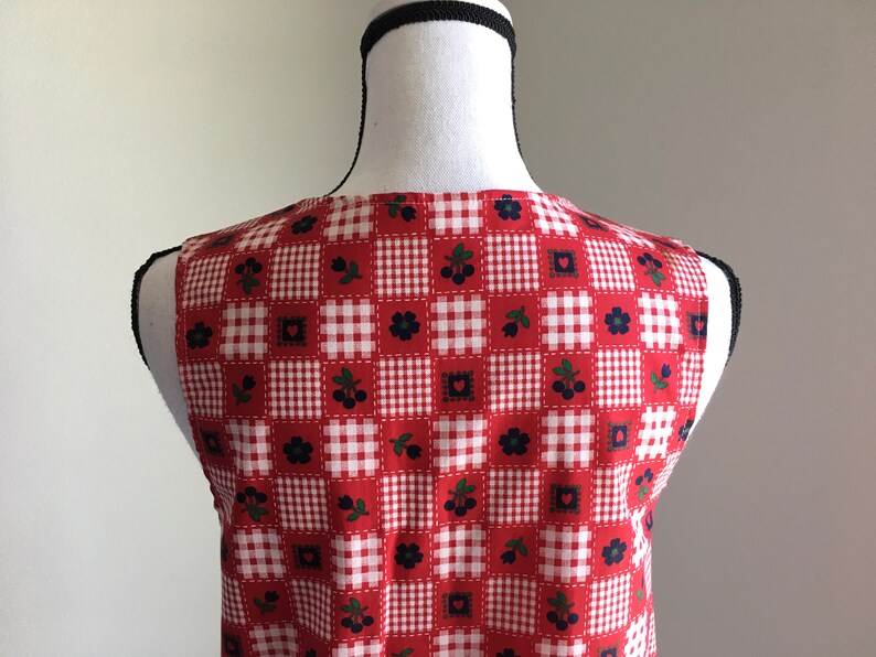 May include: Red and white gingham sleeveless vest with a patchwork design featuring small red hearts, black flowers, and green leaves with black berries.