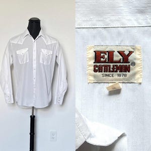 May include: A white long-sleeve shirt with a Western-style design. The shirt features two chest pockets, a pointed collar, and snap closures on the cuffs. The label reads "ELY CATTLEMAN SINCE 1878".