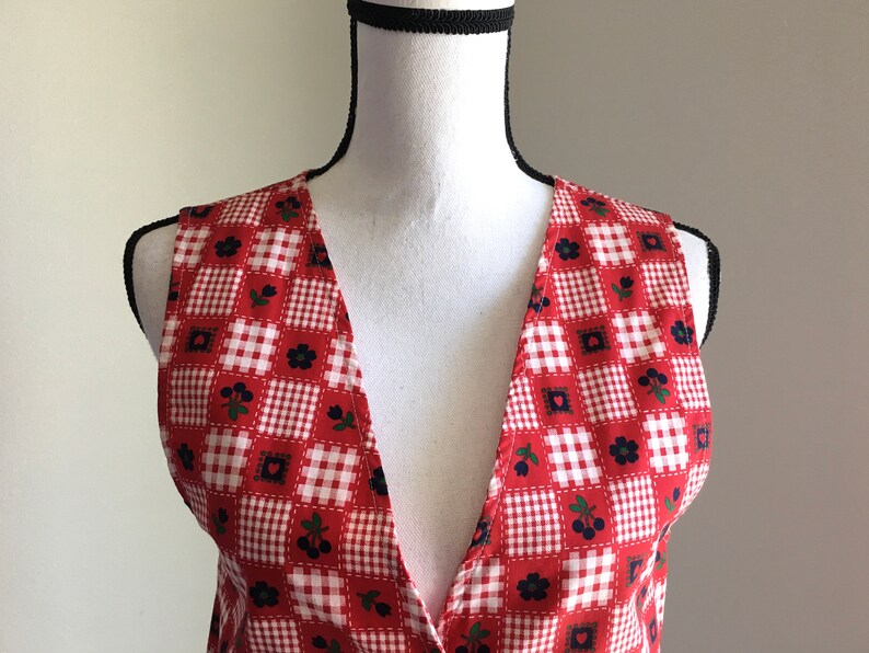 May include: A red and white gingham sleeveless vest with a deep V-neck and a floral pattern.