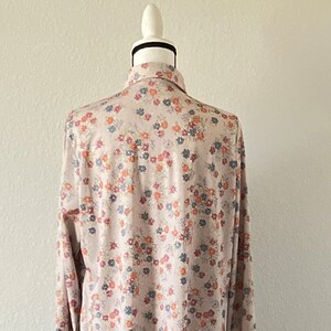 Puede incluir: Una camisa beige de manga larga con estampado floral de peque&ntilde;as flores azules, naranjas y rosas.