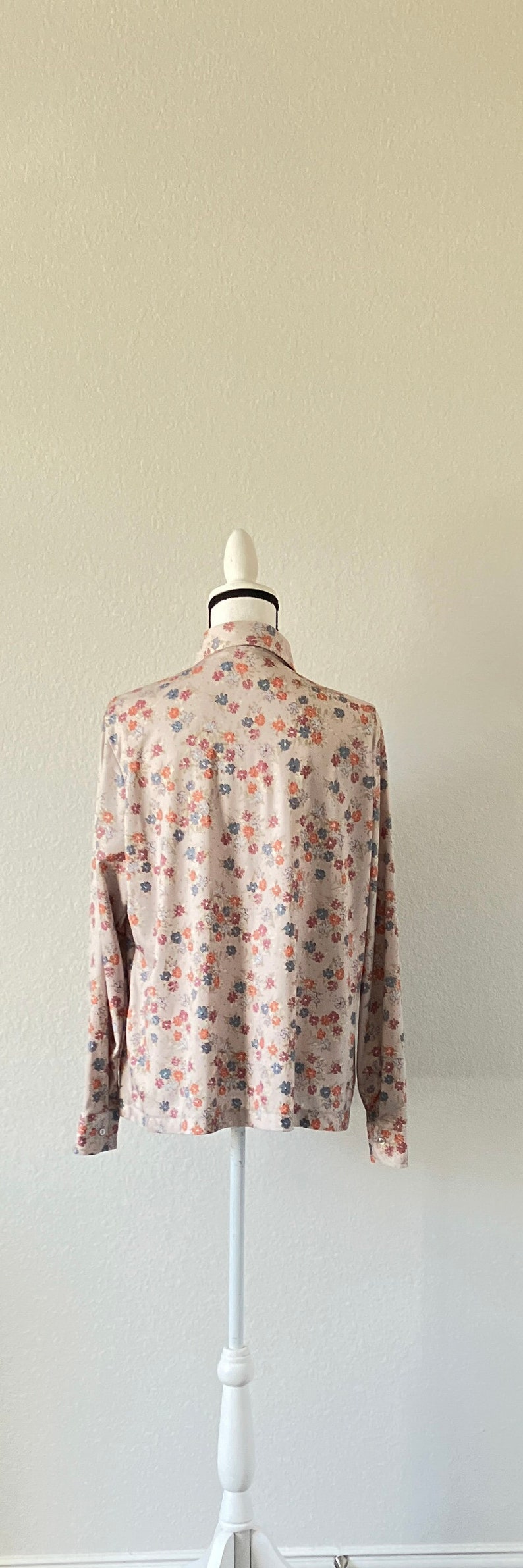 Puede incluir: Una camisa beige de manga larga con estampado floral de peque&ntilde;as flores azules, naranjas y rosas.