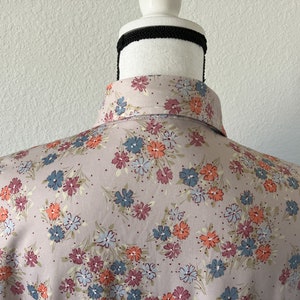 Puede incluir: Una camisa de botones rosa claro con estampado floral. Las flores son en tonos de azul, naranja y rosa.
