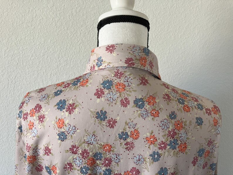 Puede incluir: Una camisa de botones rosa claro con estampado floral. Las flores son en tonos de azul, naranja y rosa.
