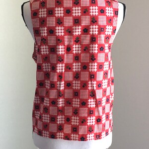 May include: A sleeveless red and white gingham vest with a floral pattern. The vest is on a white mannequin.