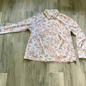 Puede incluir: Una camisa de manga larga con botones, fondo blanco y estampado floral en tonos azules, rosas y naranjas.