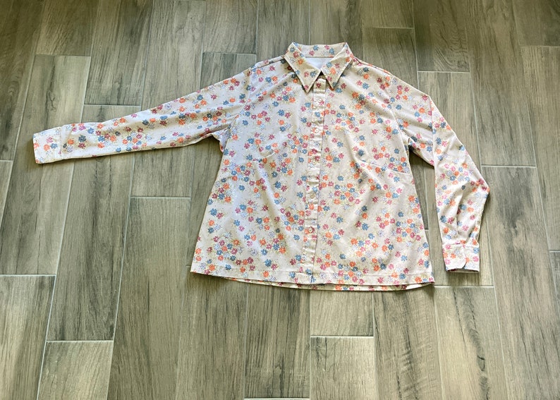 Puede incluir: Una camisa de manga larga con botones, fondo blanco y estampado floral en tonos azules, rosas y naranjas.