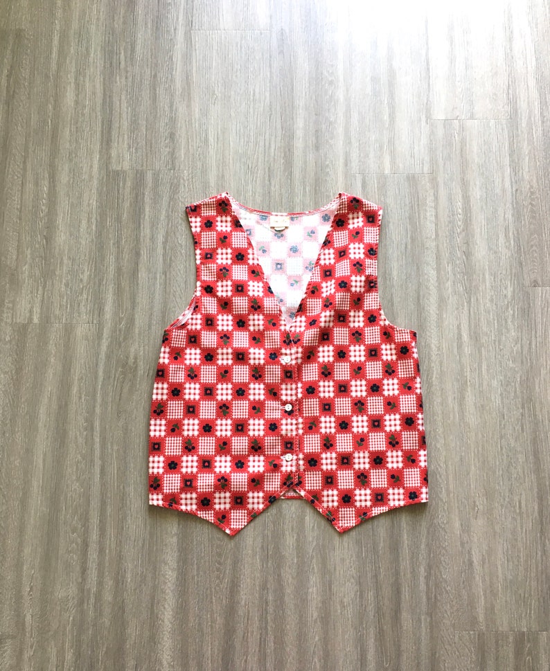 May include: A red and white checkered vest with a floral pattern. The vest has a V-neck and a button closure.